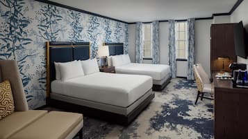 A hotel room with two beds, a desk, a chair, a TV, and a window with curtains.