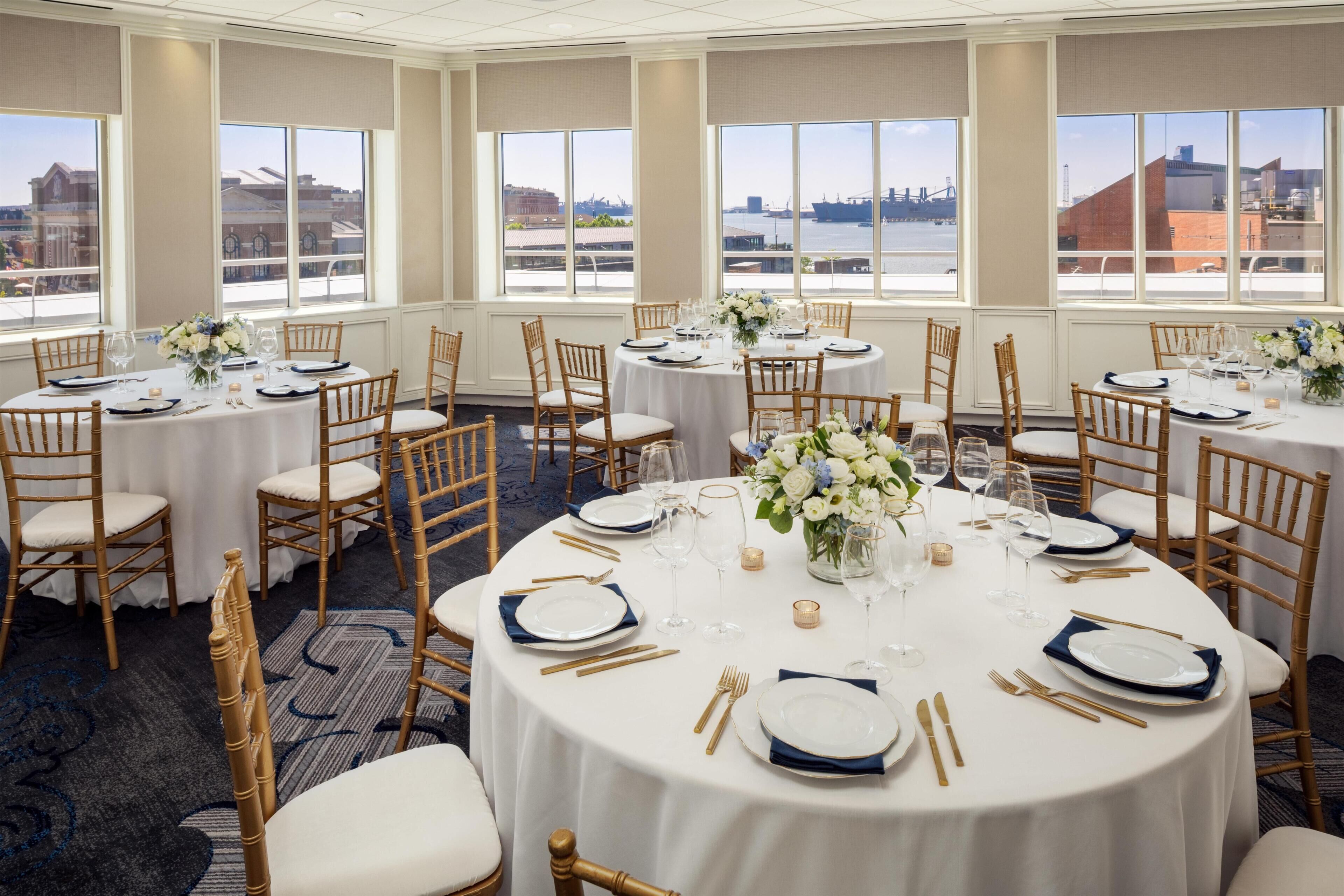 A hotel dining area with round tables, chairs, and views of a waterfront.