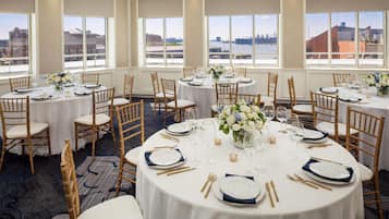 A hotel dining area with round tables, chairs, and views of a waterfront.