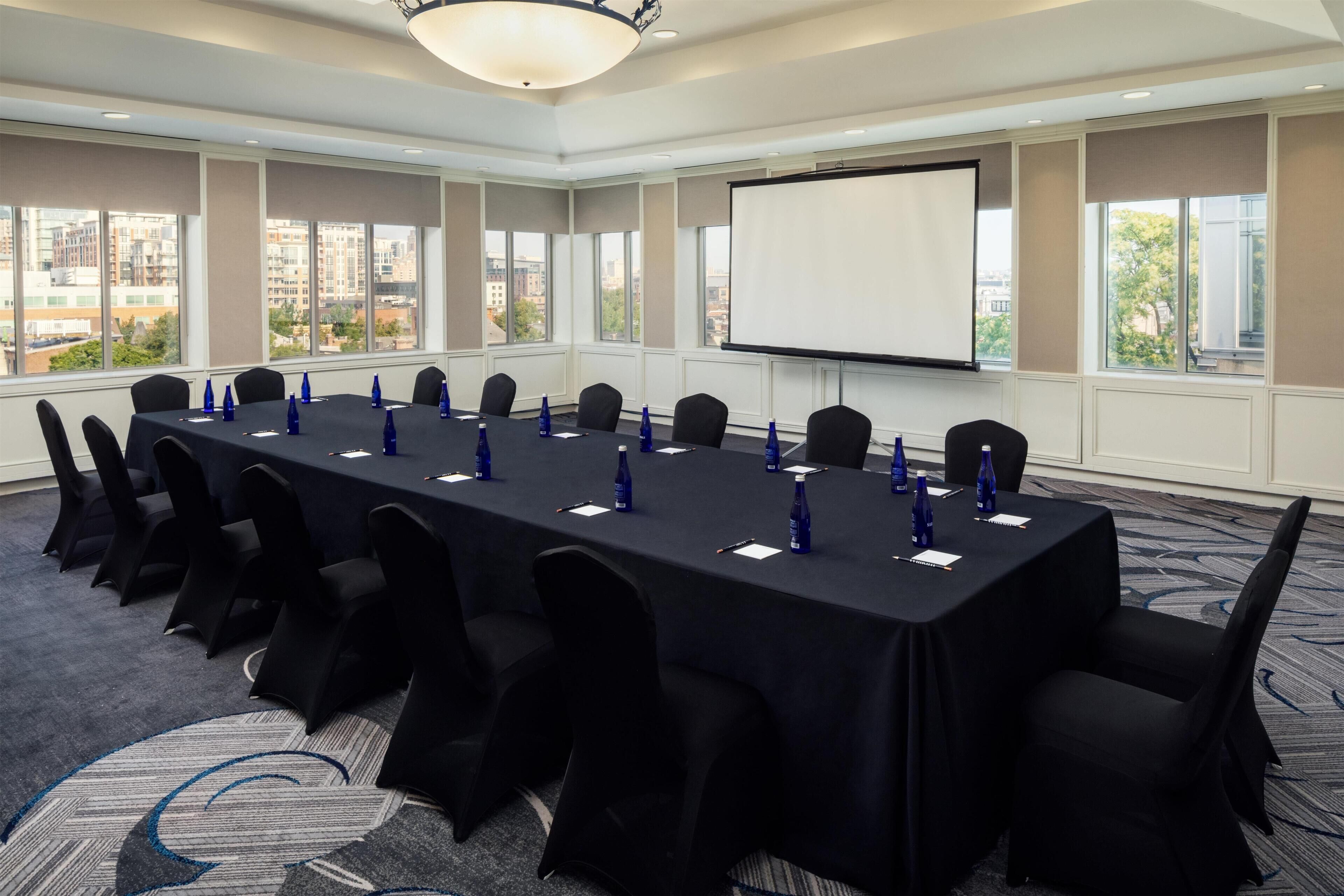 A conference room with a long table, chairs, a projector screen, and large windows.