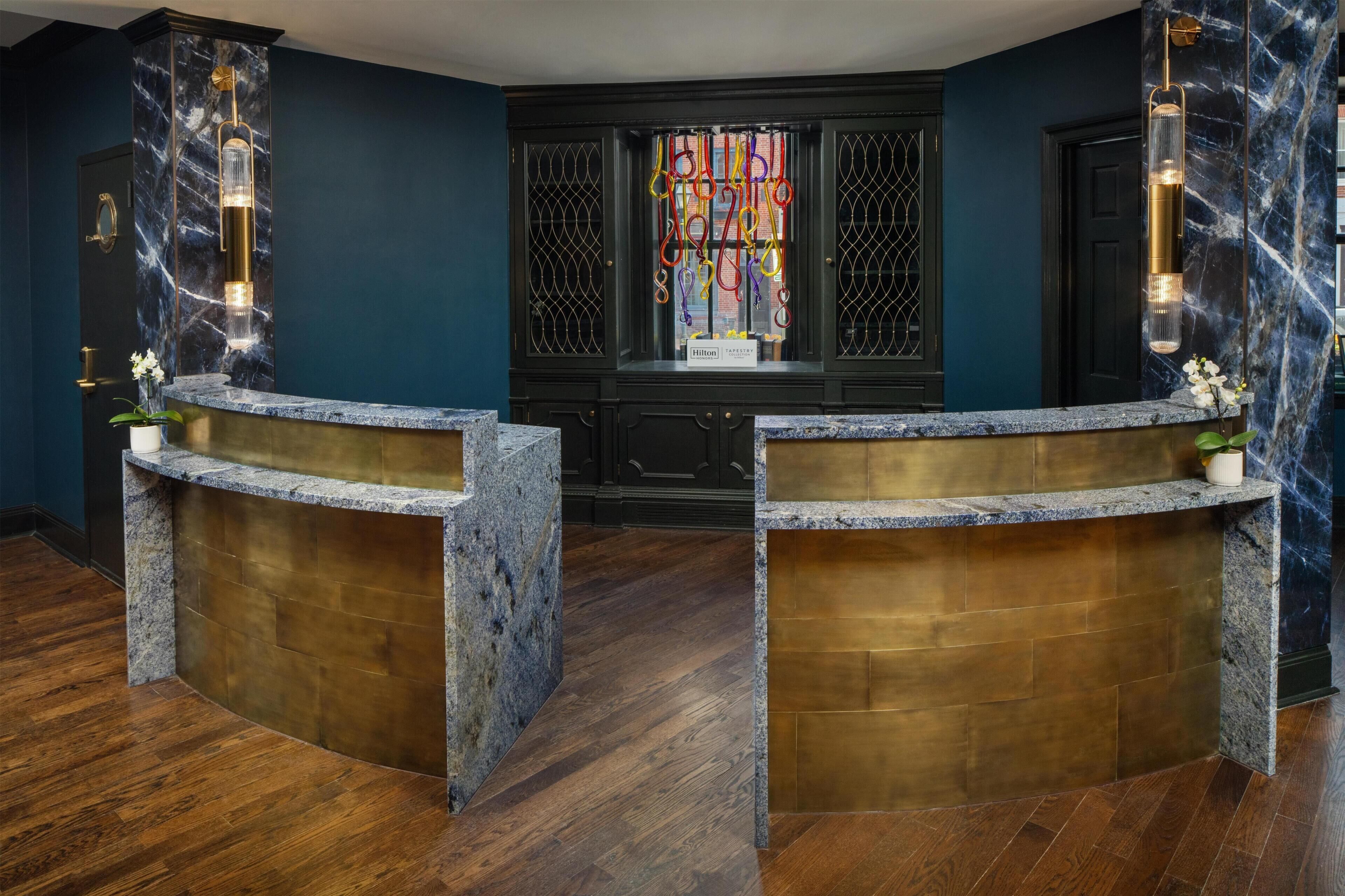 A reception desk with marble and wood finishes, a dark blue wall, and a window with colorful curtains.
