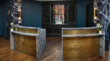 Een receptiebalie met marmeren en houten details, een donkerblauwe wand en een raam met kleurrijke gordijnen.