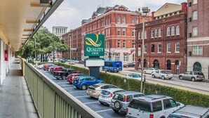 A parking lot with cars, a Quality Inn sign, and red brick buildings in the background. - Quality Inn Savannah Historic District (Savannah)