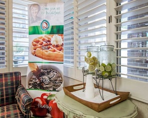 A breakfast setup with a poster advertising a breakfast event, a tray with jars of sliced lemons and limes, and a bowl of fresh strawberries.