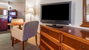 A hotel room with a flat-screen TV on a wooden dresser, a small table with a chair, a microwave, and a lamp. - Quality Inn Savannah Historic District (Savannah)