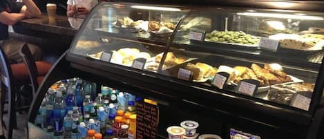 Un expositor de panadería con diversos productos horneados y una selección de bebidas.