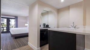 A hotel room with a bed, a small kitchenette, a dishwasher, and a view of the outside balcony.
