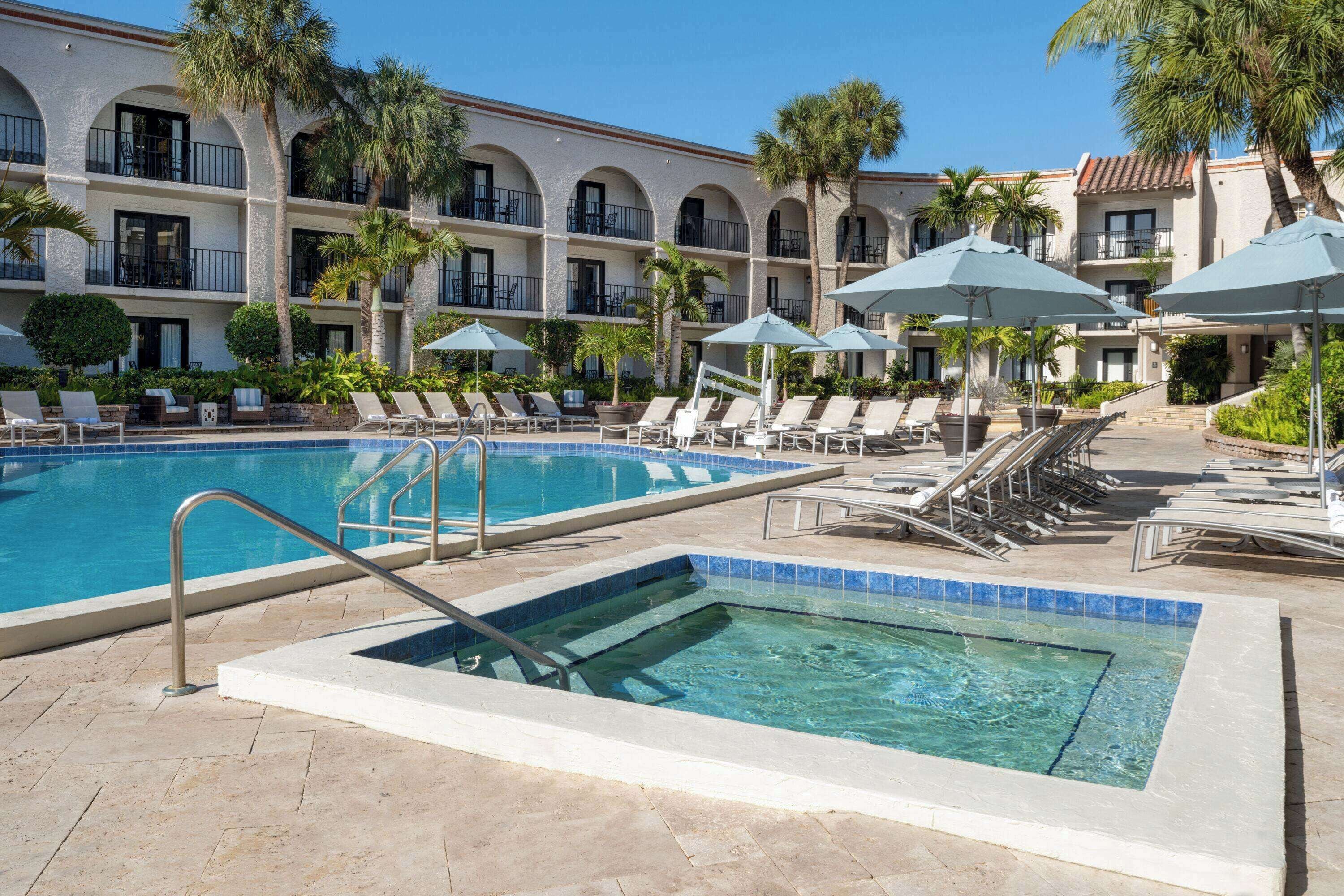 A hotel pool area with lounge chairs, umbrellas, and a clear blue pool.