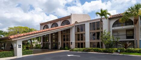 A hotel with a covered entrance, large windows, and a parking lot.