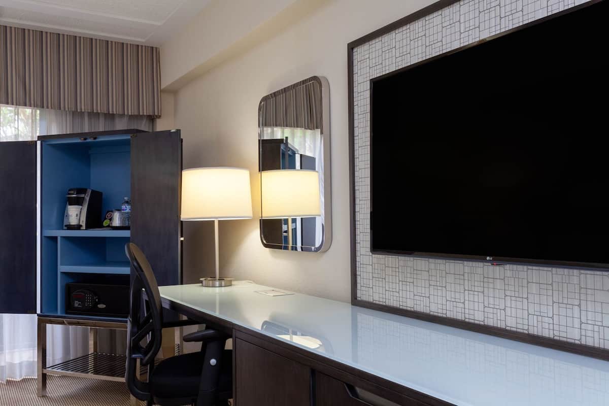 Een hotelkamer met een bureau, twee lampen, een televisie, een minibar en een zithoek.