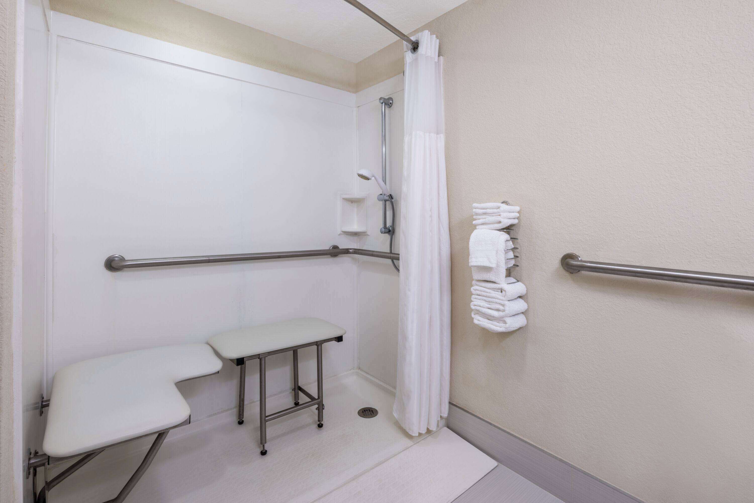 A handicap-accessible bathroom with a shower, a bench, and a towel rack.
