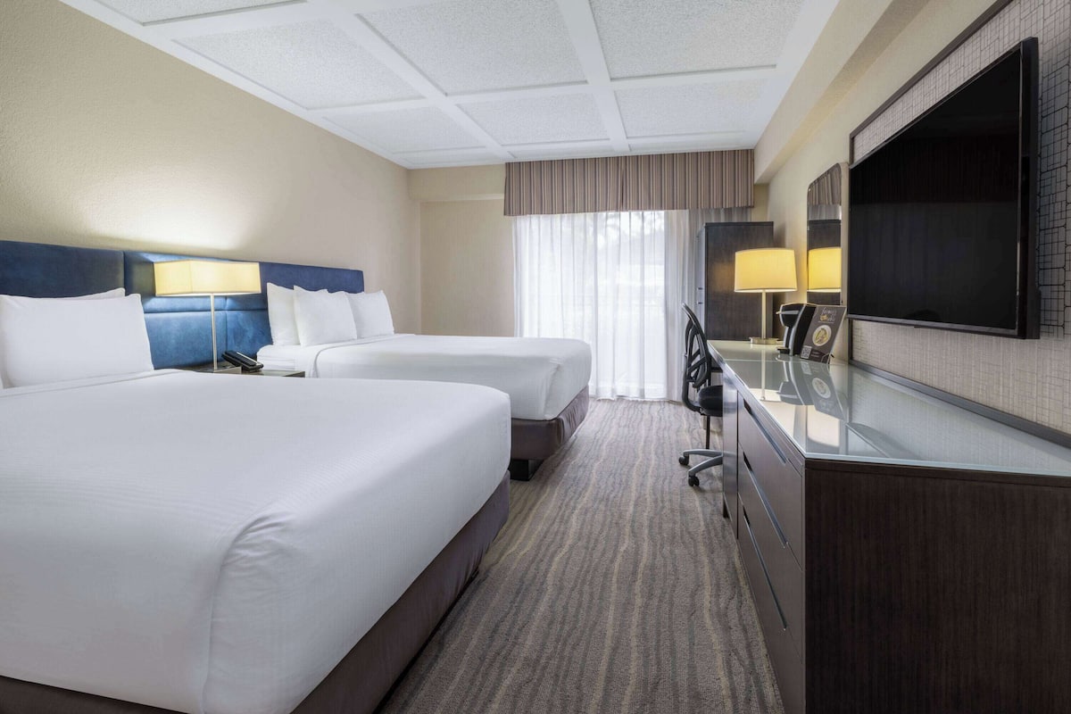 Een hotelkamer met twee bedden, een bureau met een flatscreen televisie en een groot raam met gordijnen.
