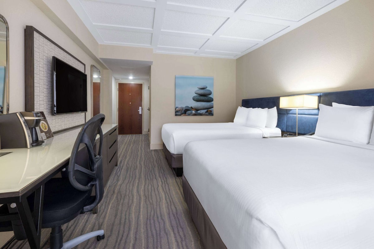 Een hotelkamer met een bureau, twee bedden, een televisie en een schilderij aan de muur.