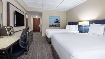 A hotel room with a desk, two beds, a television, and a painting on the wall.
