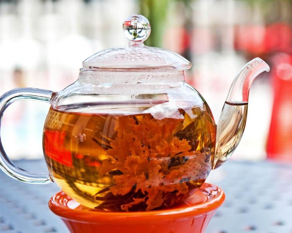 A clear glass teapot with a lid on a red saucer.