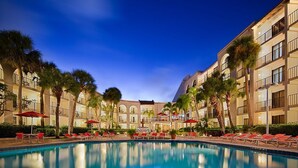 A hotel pool area with a clear view of the pool, red lounge chairs, and palm trees.