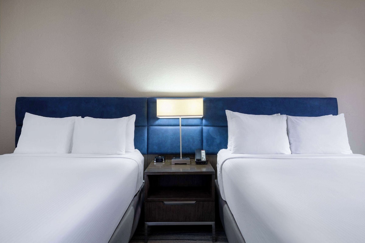 Een hotelkamer met twee bedden, een nachtkastje met een lamp en een lade.