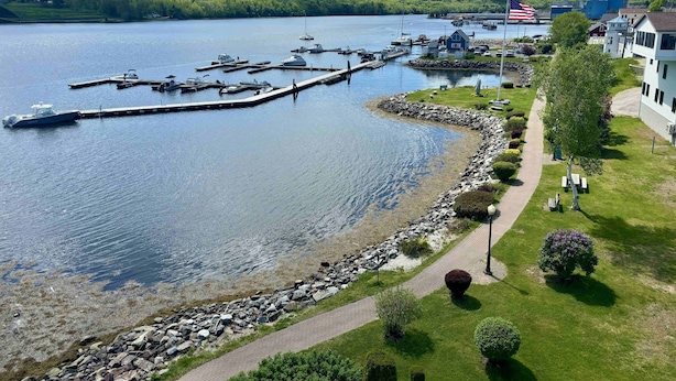 A lakeside marina with boats docked, a dock extending into the water, and a pathway along the shore.