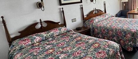 Een hotelkamer met twee houten bedden, bloemenbeddengoed, een ingelijst schilderij aan de muur en een tafeltje met een stoel.