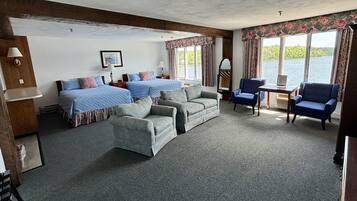 Een kamer met twee bedden, een slaapbank, twee fauteuils, een tafeltje en een raam met uitzicht op een waterpartij.