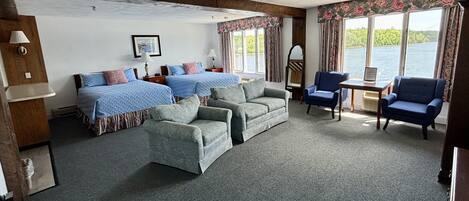 A room with two beds, a sofa, two armchairs, a small table, and a window with a view of a body of water.