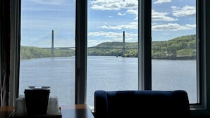 A room with a large window overlooking a river and a bridge. There is a table with a basket and a glass.