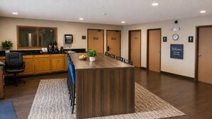 Una sala de conferencias con una larga mesa, sillas, un área de cocina con armarios y electrodomésticos, y un reloj en la pared.