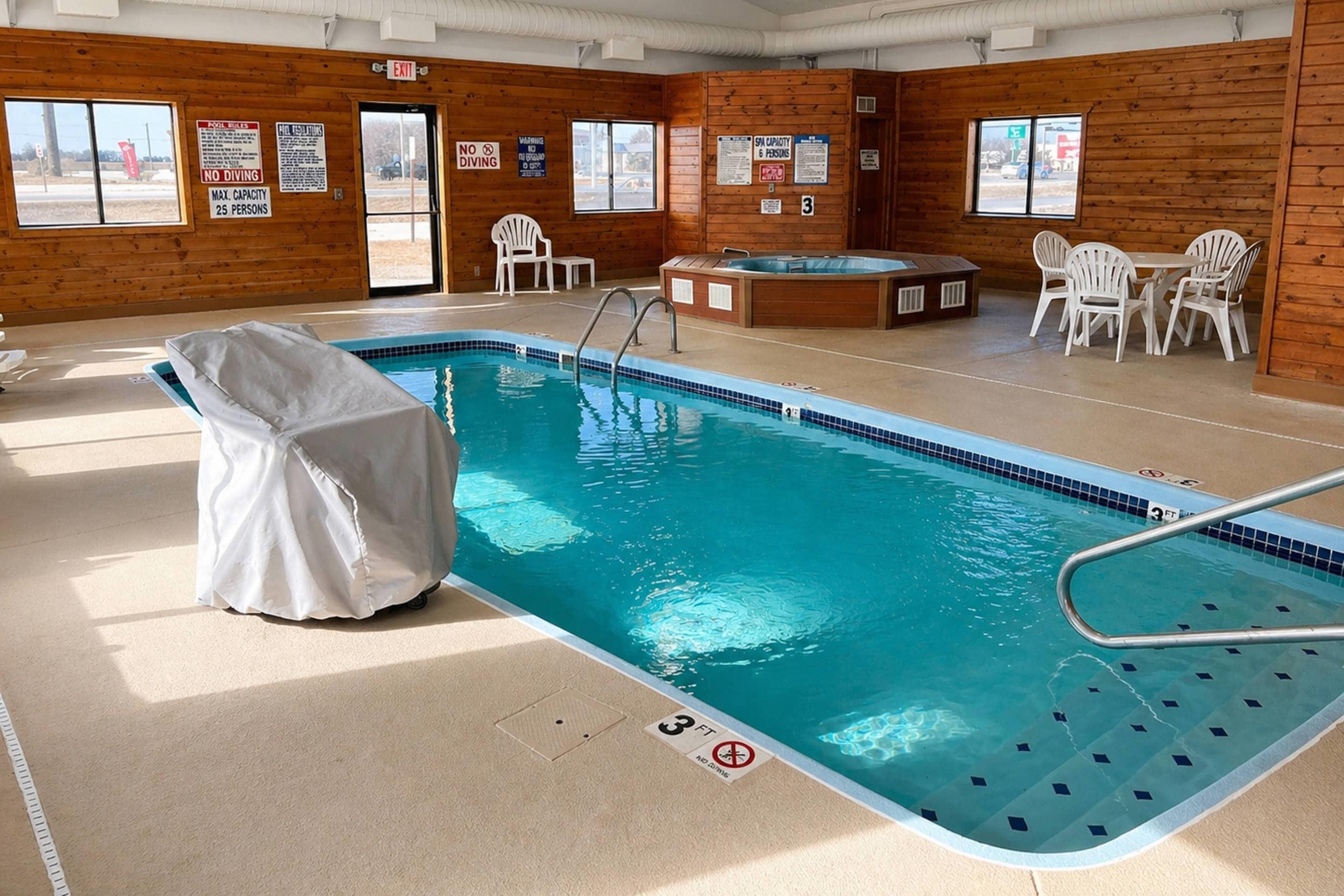 Una piscina interior con una silla techada, un jacuzzi y una mesa con sillas.