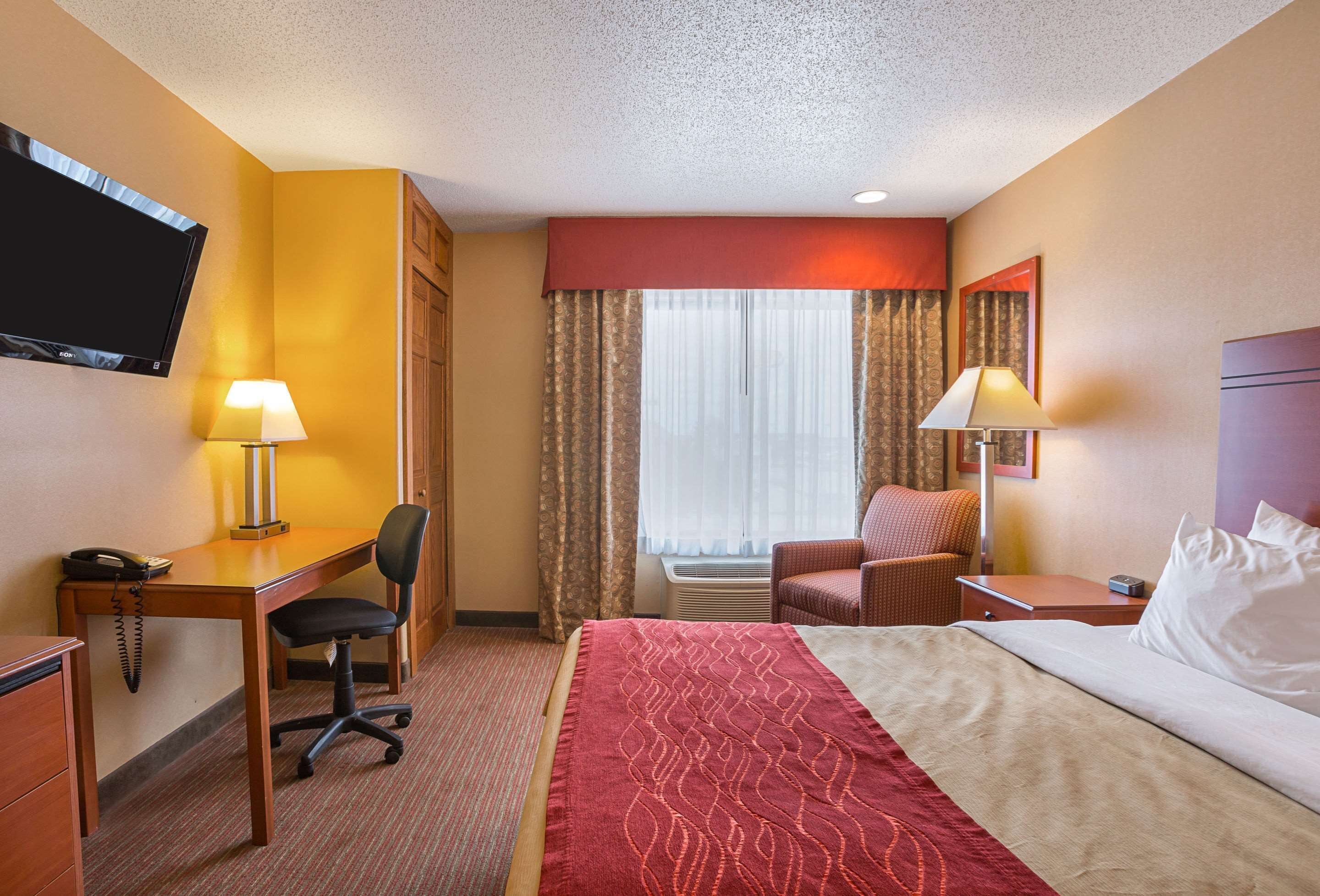 A hotel room with a bed, desk, chair, television, and lamps.