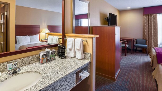 Habitación de hotel con una cama grande, un tocador con espejo, un lavabo, una cafetera y un televisor.