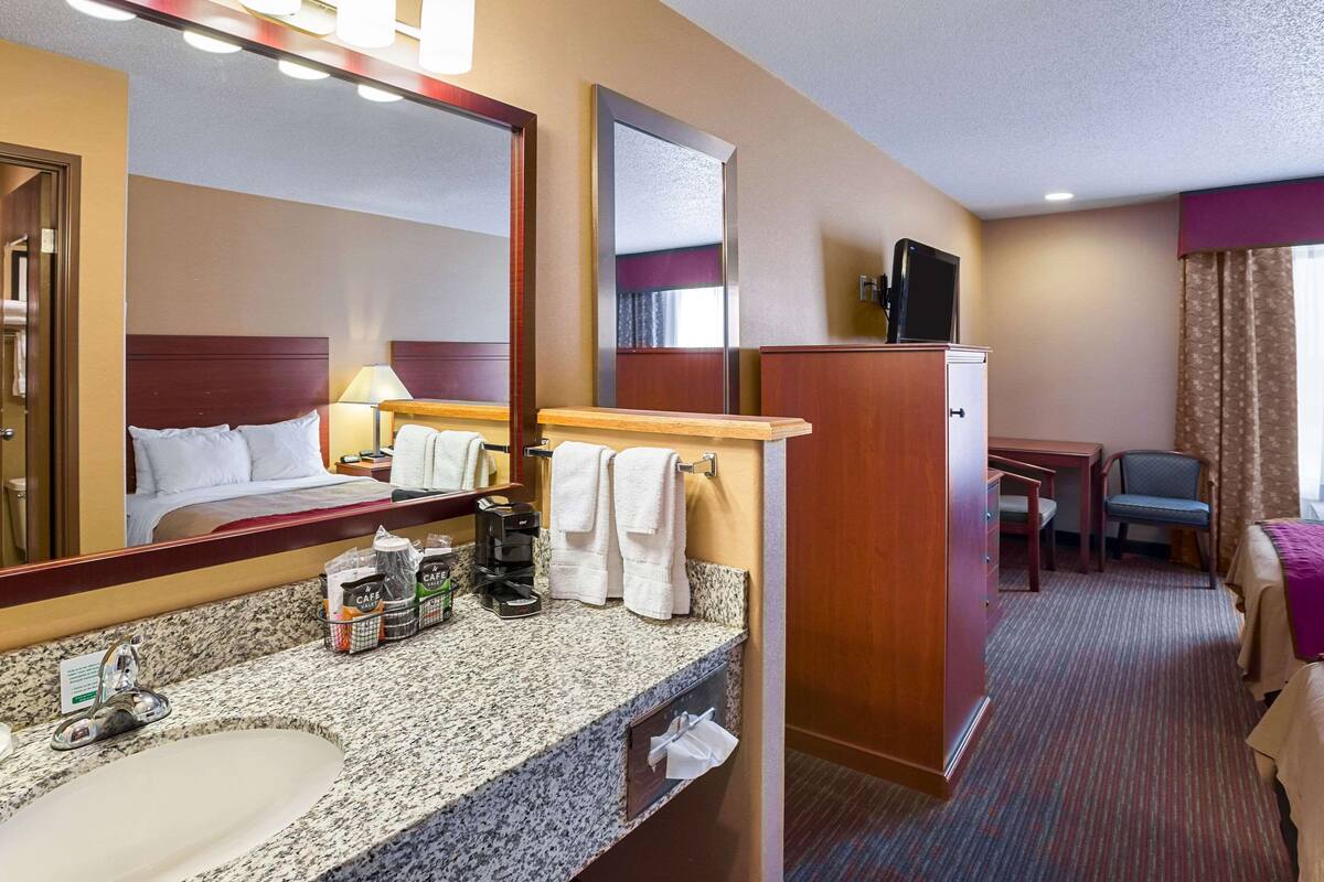 A hotel room with a large bed, a vanity with a mirror, a sink, a coffee maker, and a television.