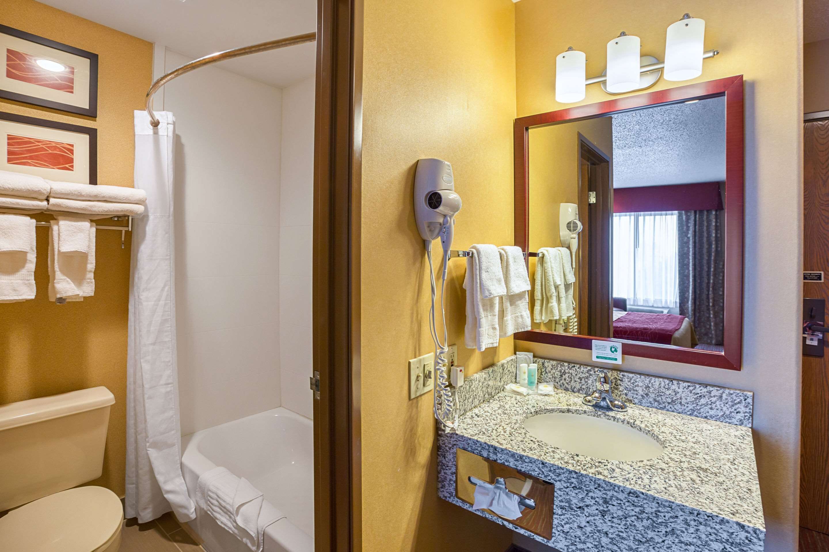 A hotel bathroom with a shower, toilet, and sink with a mirror.