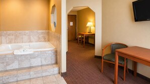 Un baño de hotel con bañera, una mesa con sillas, una lámpara y un televisor de pantalla plana.