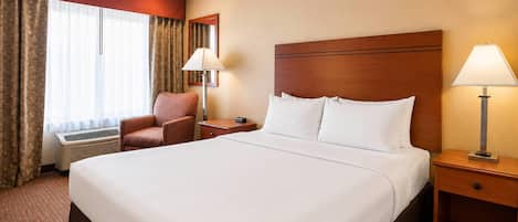 A hotel room with a large bed, a chair, a nightstand, a lamp, and a window with curtains.