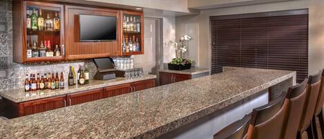 A kitchen with a granite countertop, wooden cabinets, a built-in TV, and a bar area with stools.