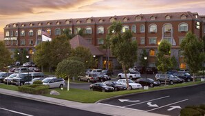 Un hotel con fachada de ladrillo, numerosas ventanas y un estacionamiento con varios coches.