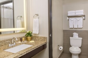 Un baño con encimera de granito, lavamanos, espejo, inodoro y toallero con varias toallas.
