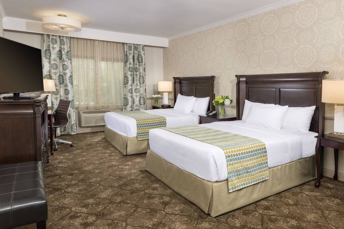 A hotel room with two beds, a desk, and a TV.