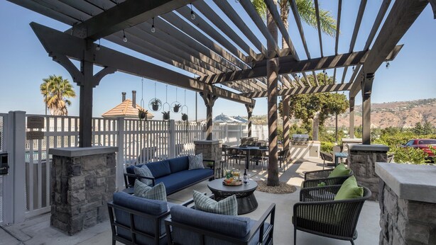 Un patio exterior con pérgola, asientos de piedra y vista a la montaña.