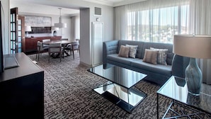 A modern hotel room with a living area, a dining area, and a view of the city.