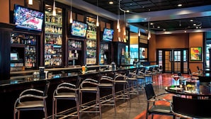 A bar area with multiple TVs, bar stools, and a variety of liquor bottles.