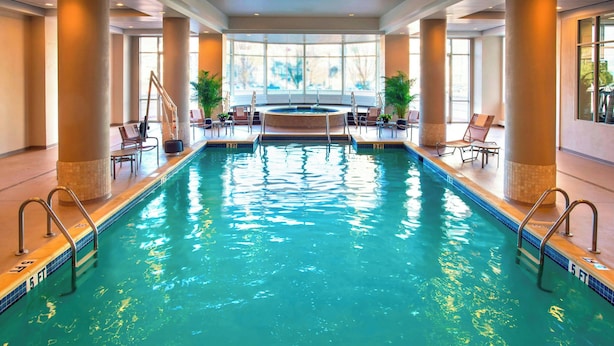 A large indoor swimming pool with clear water, surrounded by lounge chairs and potted plants.