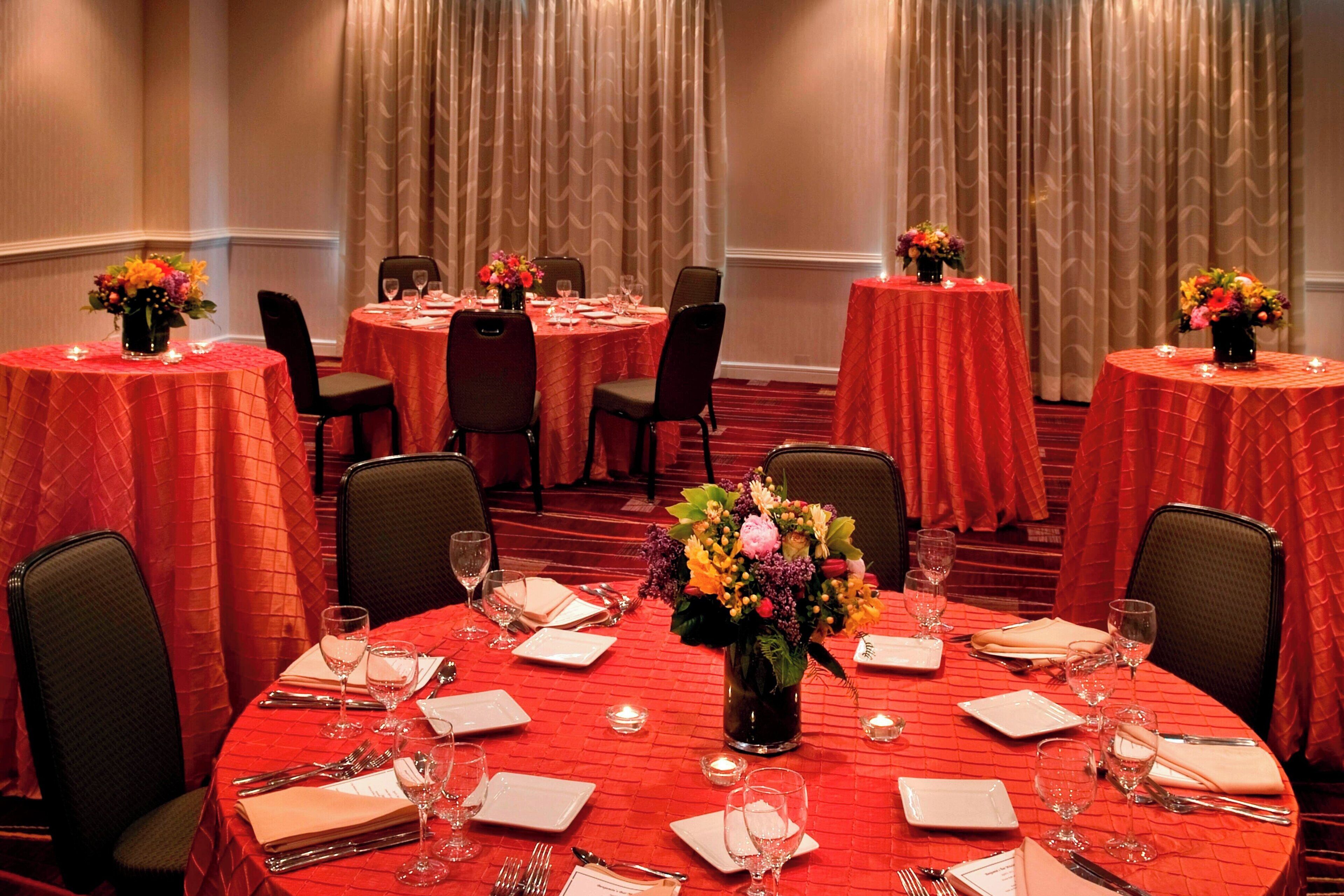 A banquet hall with multiple round tables, each set with white plates, cutlery, and glasses.