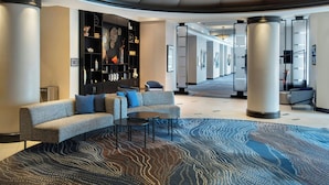 A modern lobby with a curved sofa, round tables, a patterned rug, and a decorative wall with shelves.