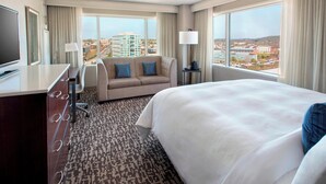A hotel room with a large bed, a sofa, a desk with a TV, and a view of the city.