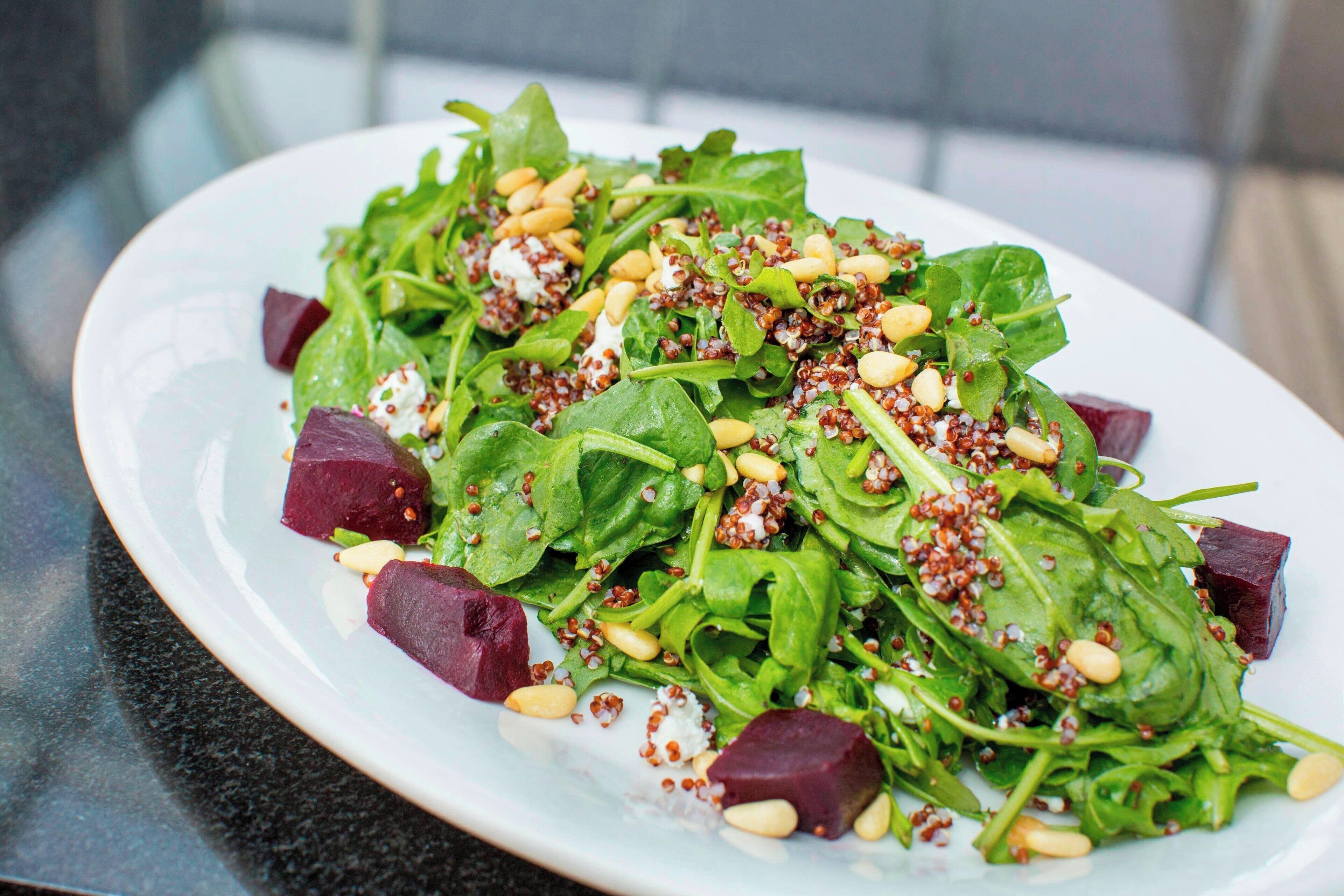 A plate of salad with greens, beets, and pine nuts.