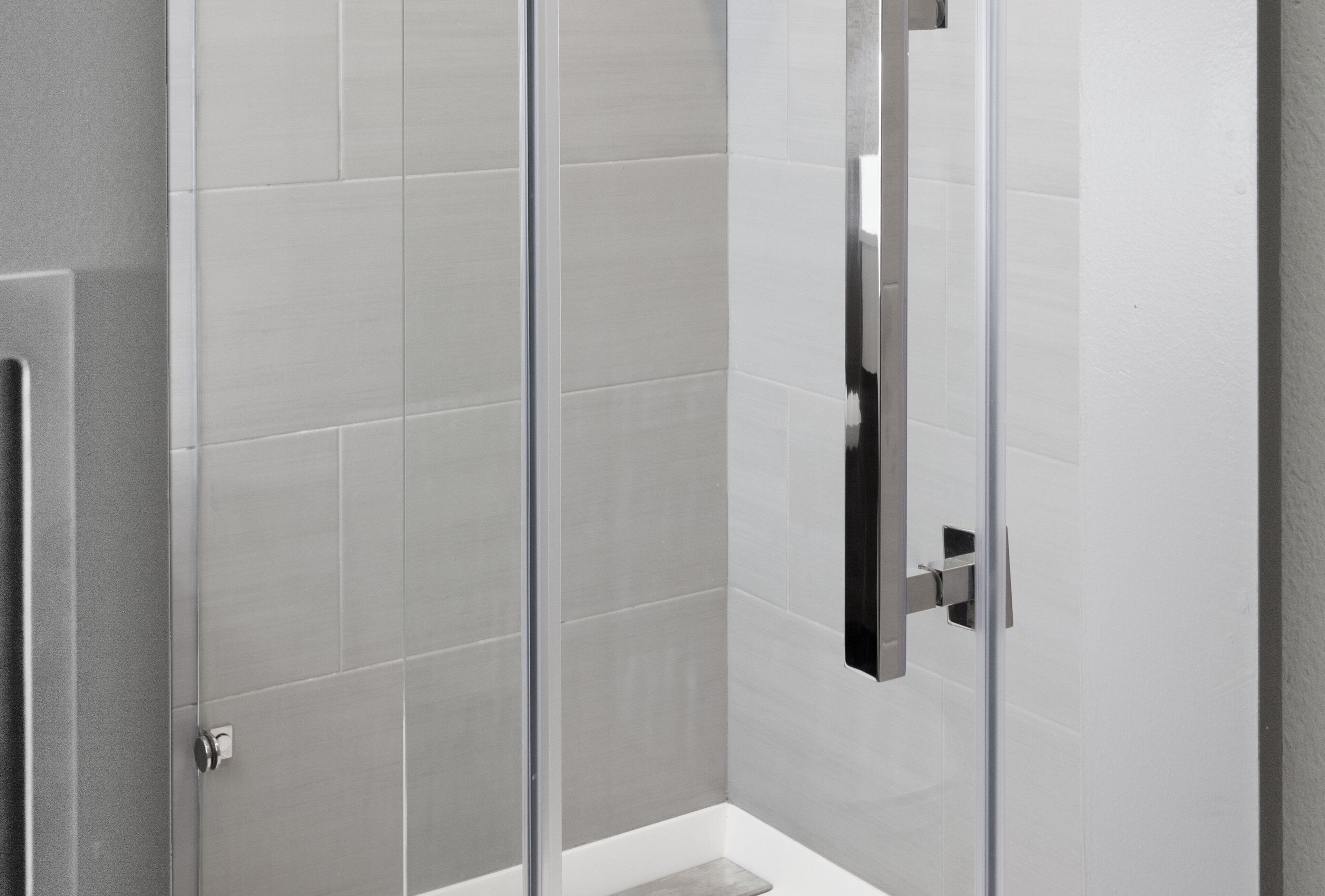 A modern bathroom with a glass shower enclosure, white tiled walls, and a metallic handle.