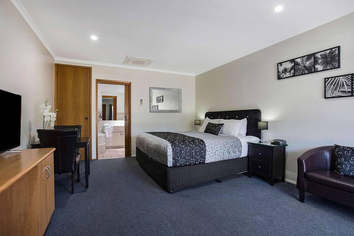 A bedroom with a bed, bedside table, lamp, TV, and a desk with a chair.