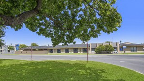 Un motel con un estacionamiento, una carretera y un árbol en primer plano.