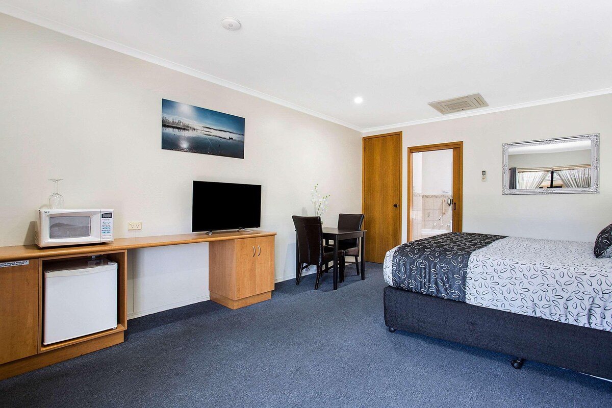 Una habitación de hotel con cama, escritorio, computadora, microondas y refrigerador.